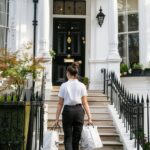 a professional female house cleaner walking up stone steps towards the front door of a grand Victorian townhouse in Kensington, London